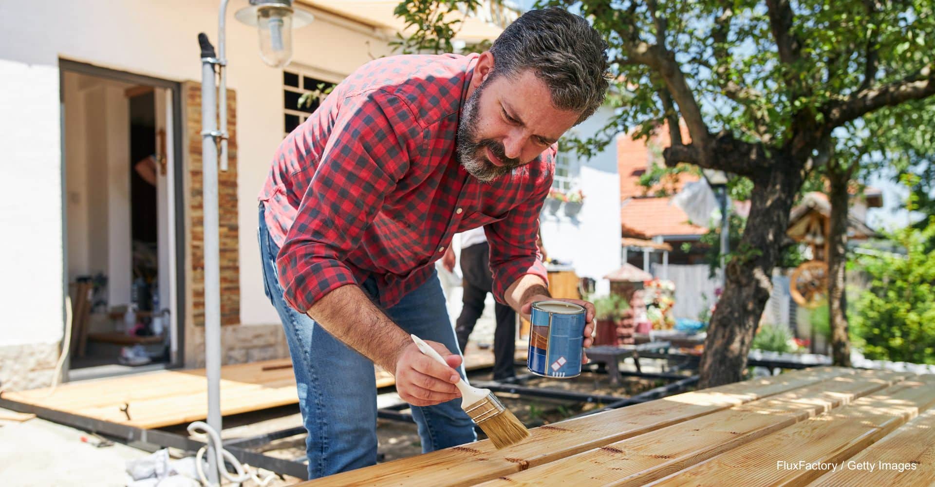 Mann steht im Garten und lasiert Holzbalken