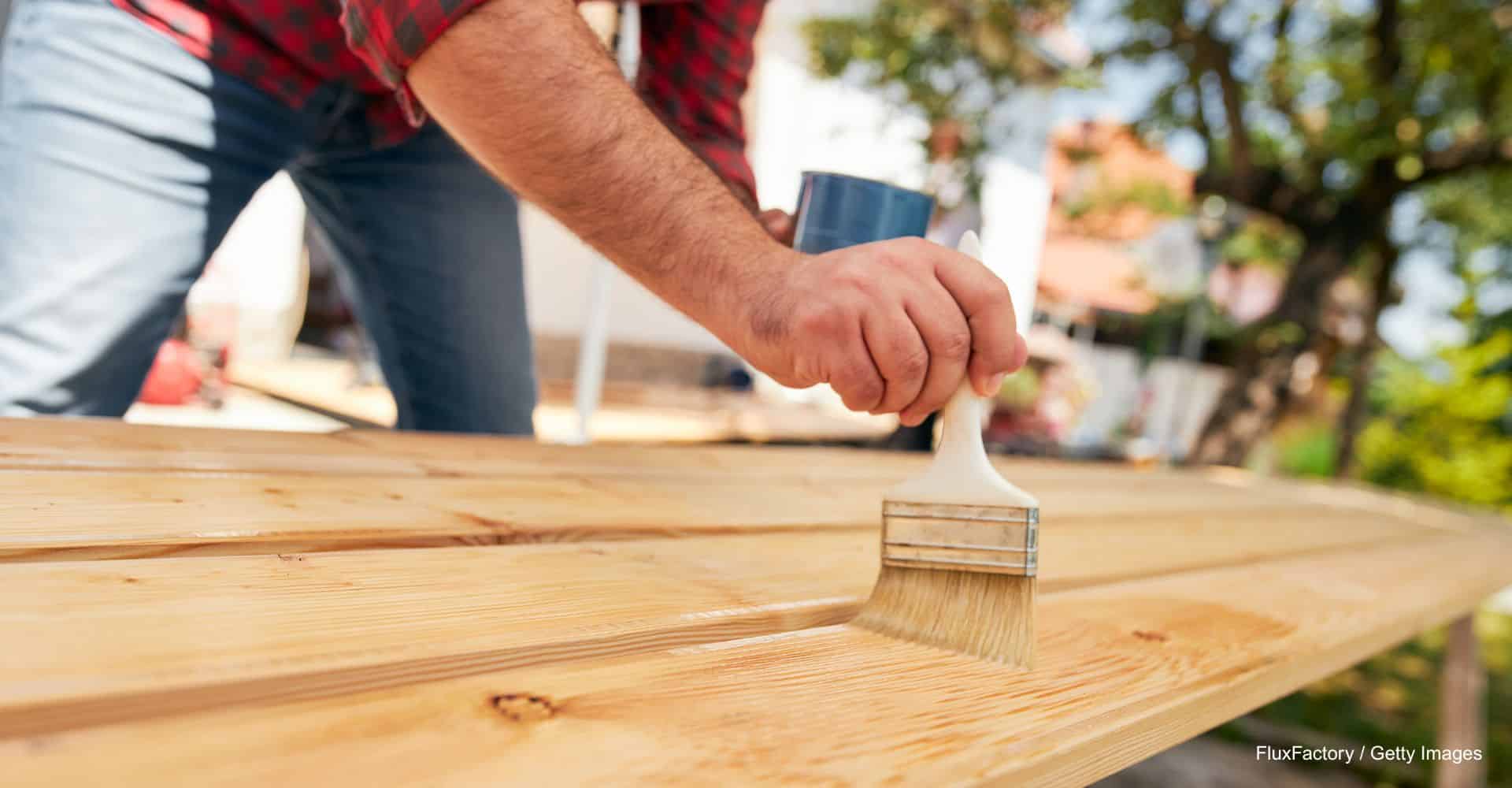 Person trägt mit einem Pinsel Lasur auf Holzfläche auf