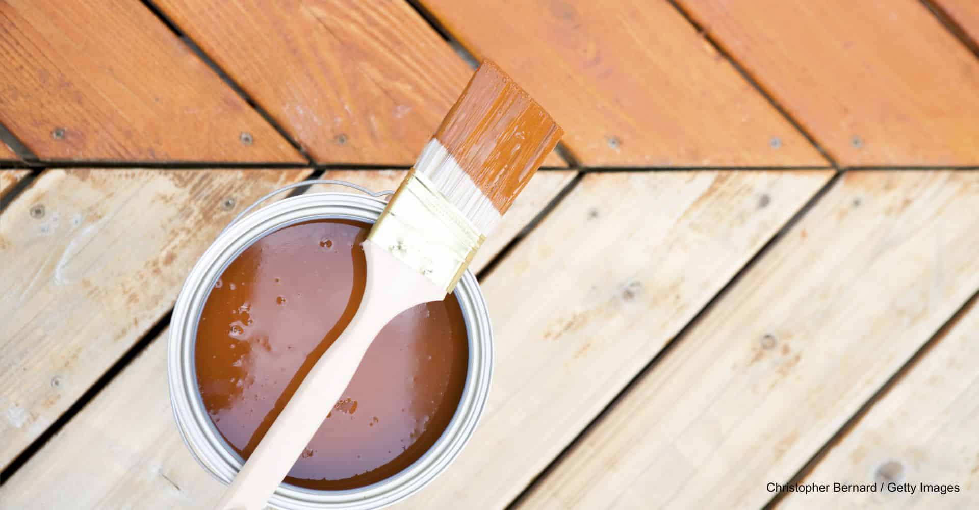 Vergleich von unbehandelten Terrassendielen und frisch mit Holzpflege behandelten Dielen und einem Eimer Pflegeprodukt mit Pinsel